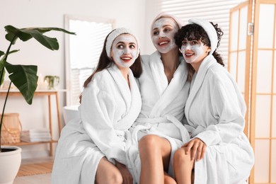 Photo of Happy friends in bathrobes with facial masks indoors. Spa party