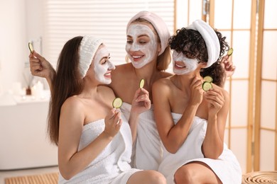 Happy friends with facial masks and cucumber slices in bathroom. Spa party