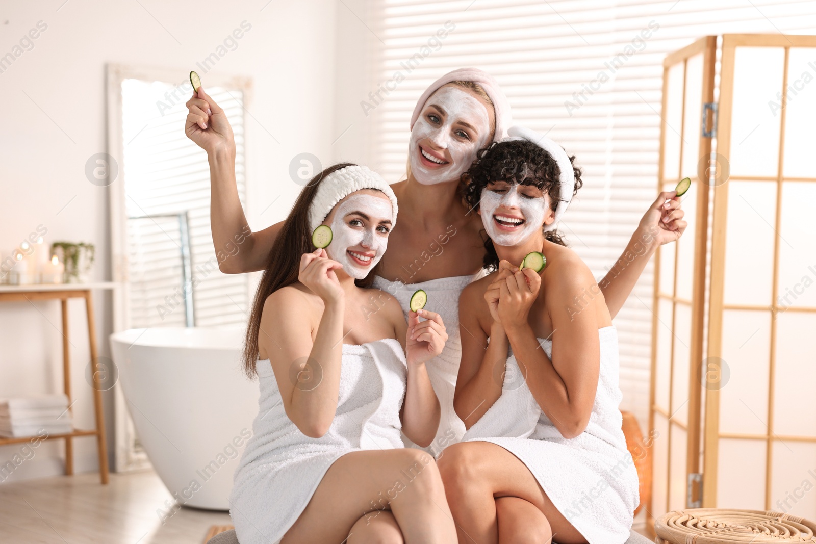 Photo of Happy friends with facial masks and cucumber slices in bathroom. Spa party