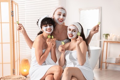 Happy friends with facial masks and cucumber slices in bathroom. Spa party