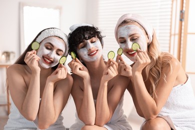 Photo of Happy friends with facial masks and cucumber slices in bathroom. Spa party