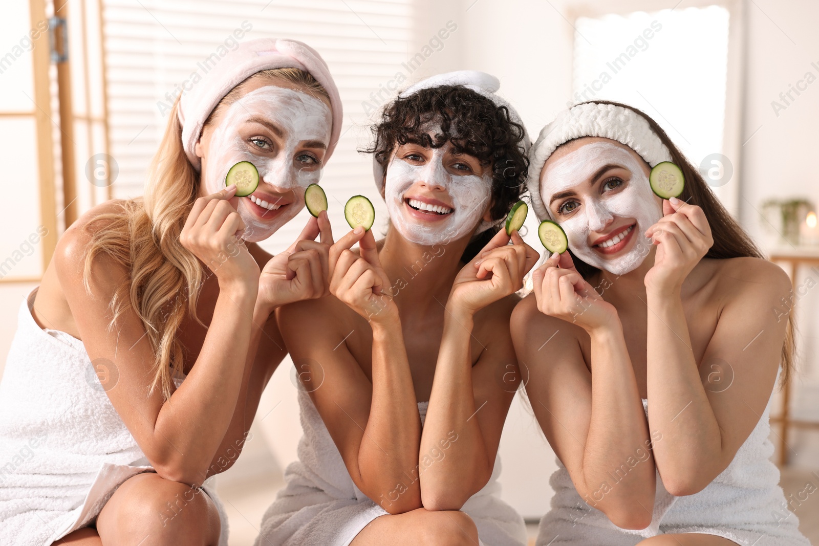 Photo of Happy friends with facial masks and cucumber slices in bathroom. Spa party