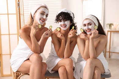 Photo of Happy friends with facial masks and cucumber slices in bathroom. Spa party