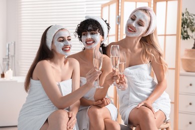 Photo of Happy friends with facial masks and glasses of sparkling wine in bathroom. Spa party