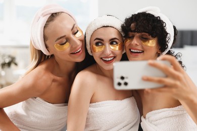Photo of Happy friends with eye patches taking selfie indoors. Spa party