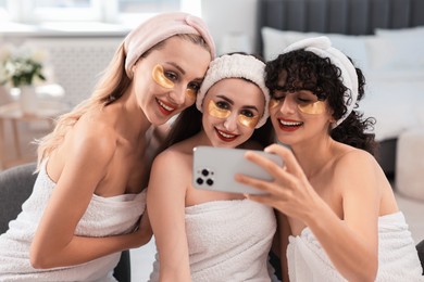 Happy friends with eye patches taking selfie indoors. Spa party