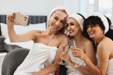 Photo of Happy friends with glasses of sparkling wine taking selfie indoors. Spa party