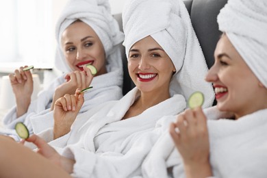 Happy friends in bathrobes with cucumber slices on bed, selective focus. Spa party