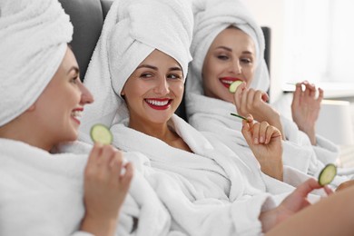 Photo of Happy friends in bathrobes with cucumber slices on bed, selective focus. Spa party