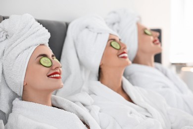 Photo of Happy friends in bathrobes with cucumber slices on bed, selective focus. Spa party