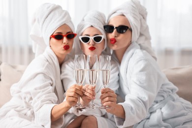 Photo of Happy friends in bathrobes with sunglasses and glasses of sparkling wine indoors, selective focus. Spa party