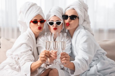 Happy friends in bathrobes with sunglasses and glasses of sparkling wine indoors, selective focus. Spa party