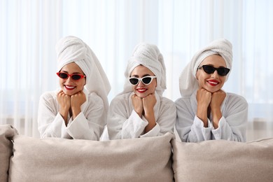 Photo of Happy friends in bathrobes with sunglasses indoors. Spa party