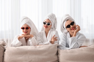 Photo of Happy friends in bathrobes with sunglasses indoors. Spa party