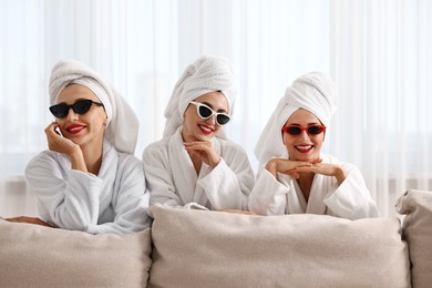 Photo of Happy friends in bathrobes with sunglasses indoors. Spa party