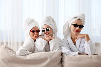 Photo of Happy friends in bathrobes with sunglasses indoors. Spa party