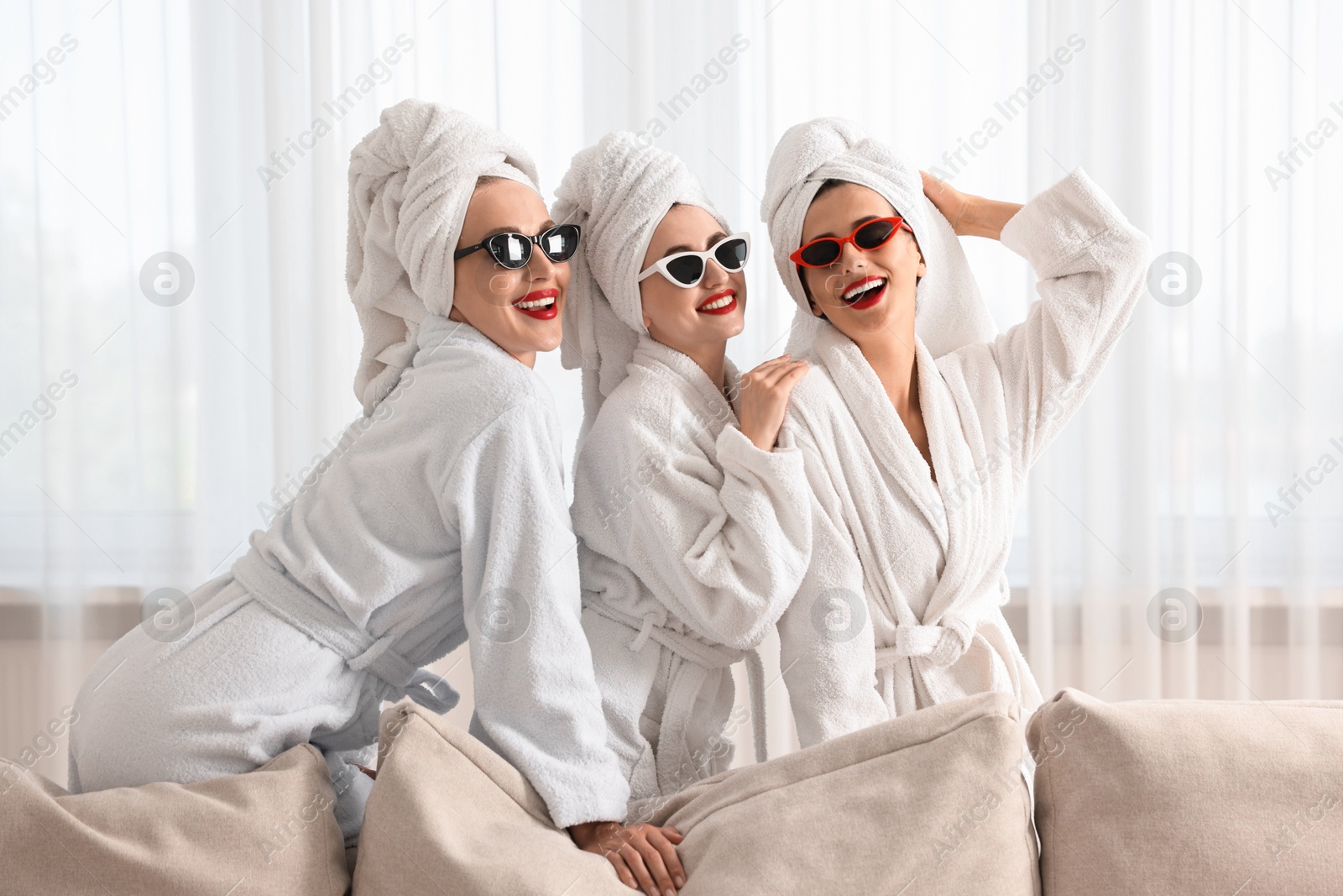 Photo of Happy friends in bathrobes with sunglasses indoors. Spa party