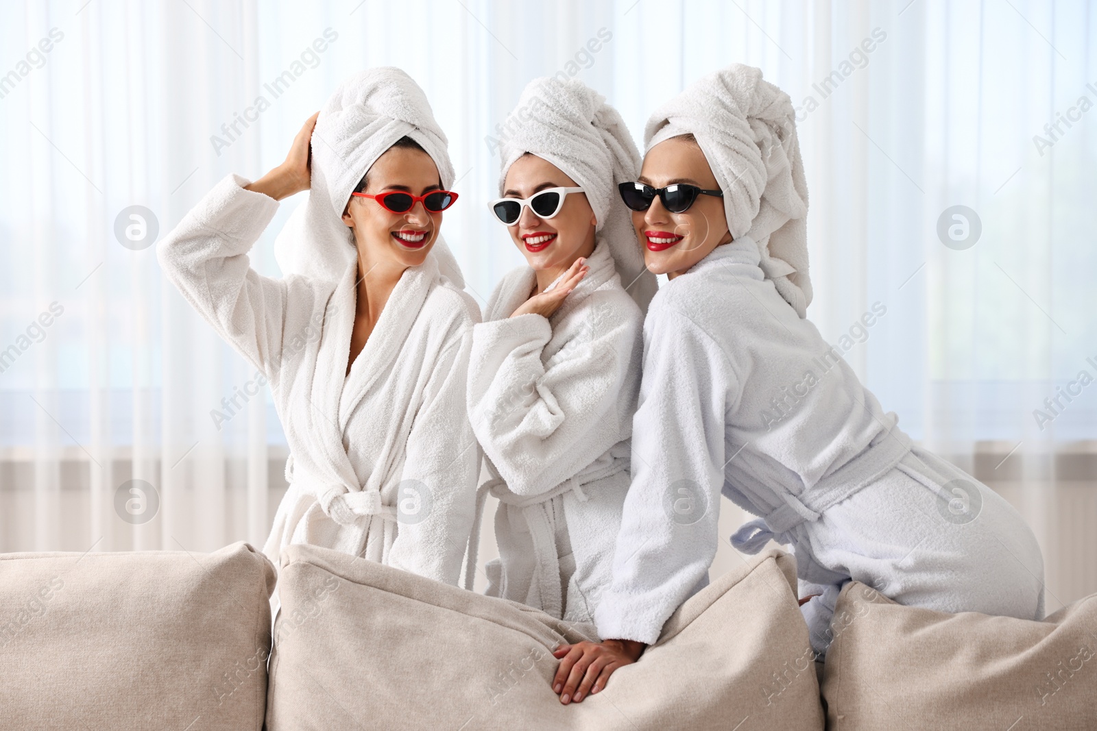 Photo of Happy friends in bathrobes with sunglasses indoors. Spa party