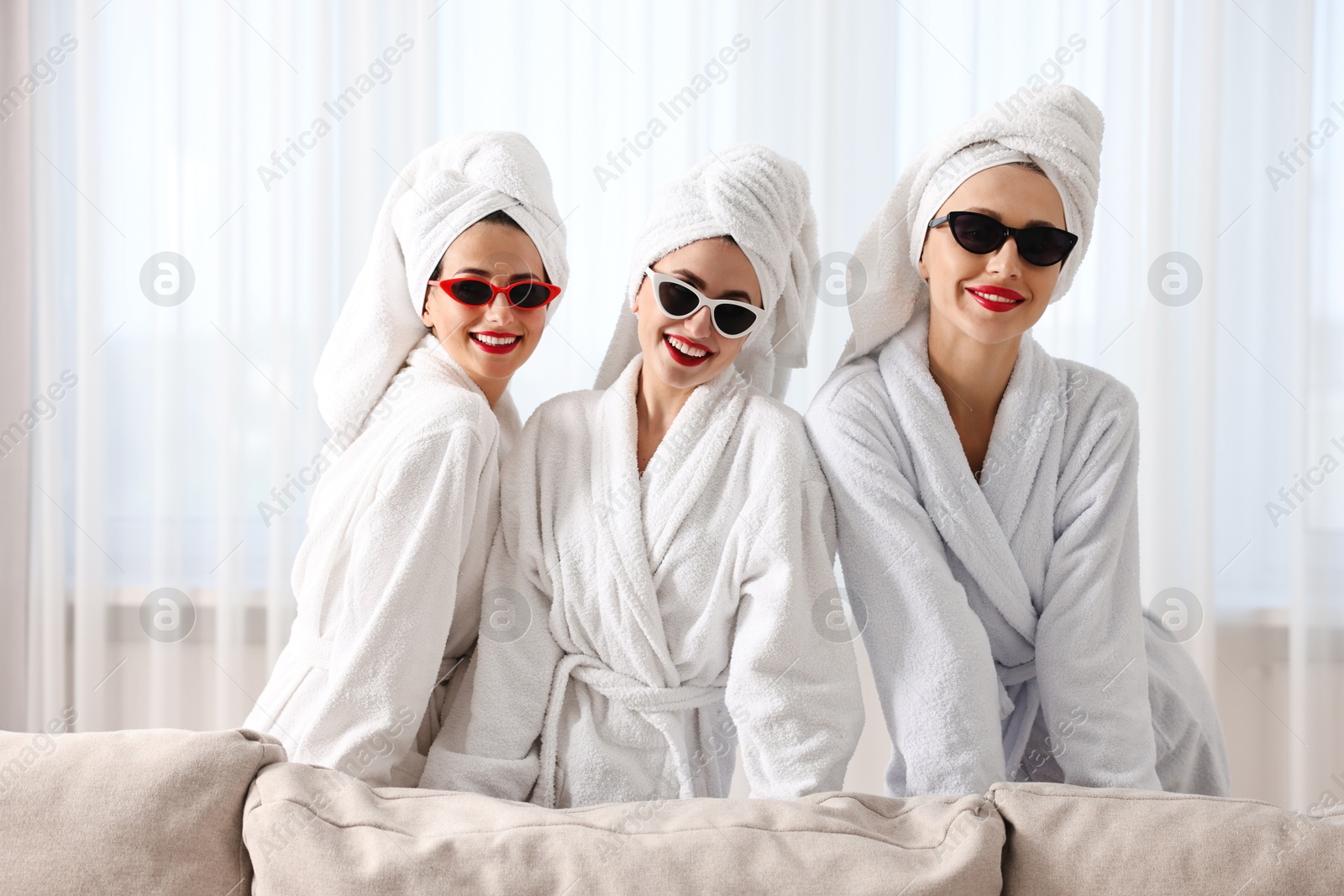 Photo of Happy friends in bathrobes with sunglasses indoors. Spa party