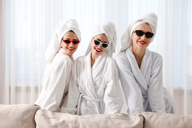 Photo of Happy friends in bathrobes with sunglasses indoors. Spa party