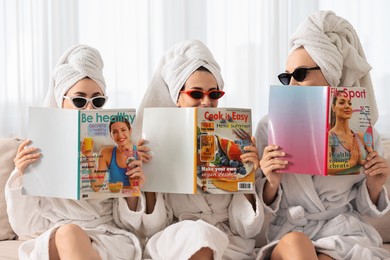 Friends in bathrobes with magazines on couch indoors. Spa party