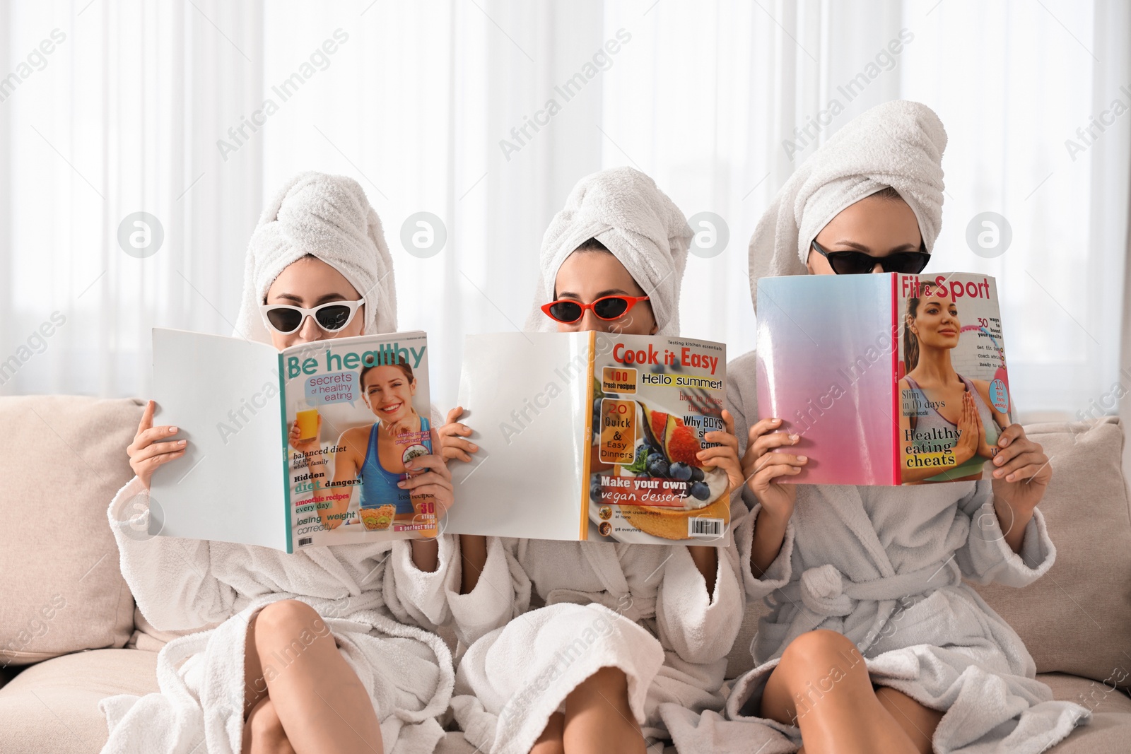 Photo of Friends in bathrobes with magazines on couch indoors. Spa party