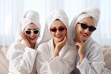 Photo of Happy friends in bathrobes with sunglasses on couch indoors. Spa party