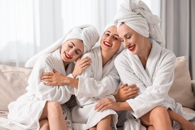 Photo of Happy friends in bathrobes with towels on couch indoors. Spa party