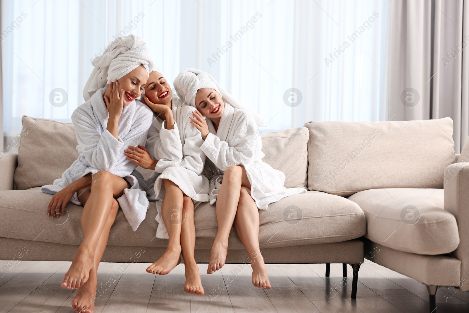 Photo of Happy friends in bathrobes with towels on couch indoors. Spa party