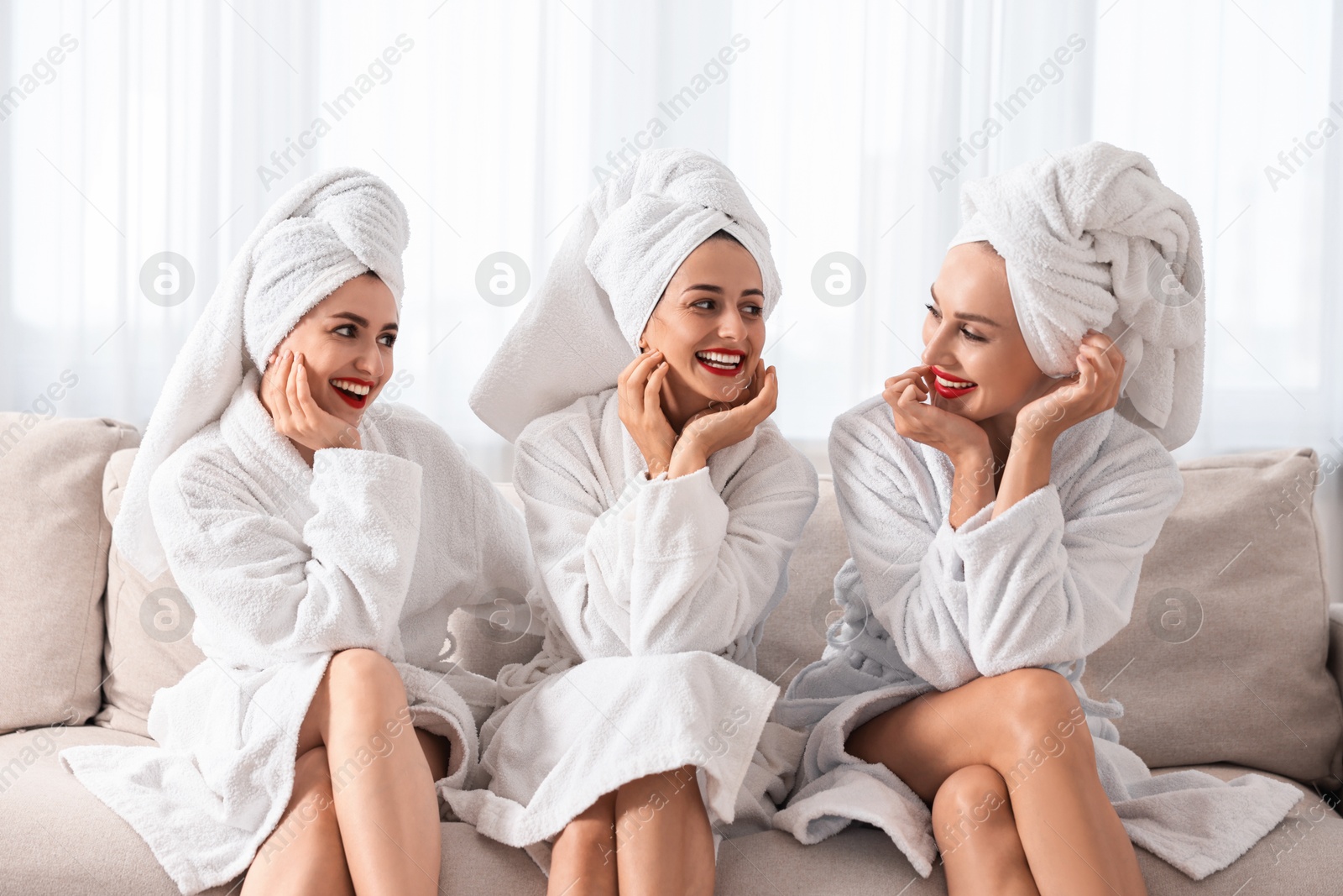 Photo of Happy friends in bathrobes with towels on couch indoors. Spa party