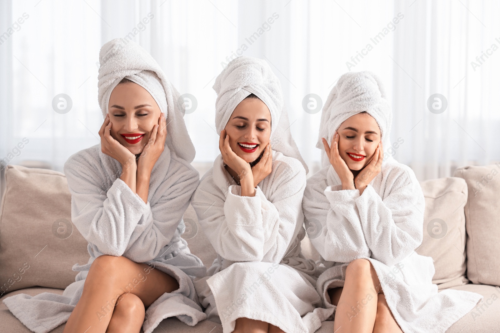 Photo of Happy friends in bathrobes with towels on couch indoors. Spa party