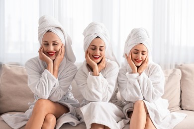 Photo of Happy friends in bathrobes with towels on couch indoors. Spa party