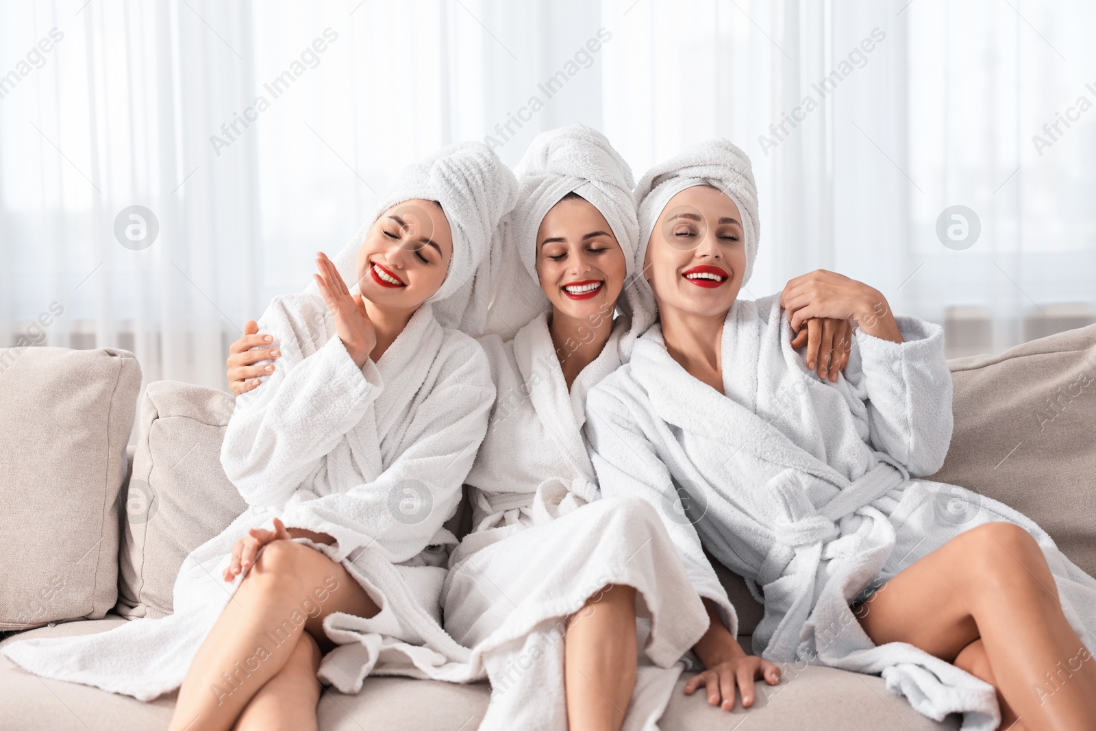 Photo of Happy friends in bathrobes with towels on couch indoors. Spa party