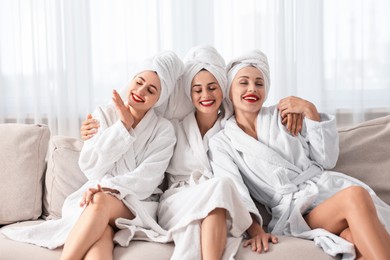 Happy friends in bathrobes with towels on couch indoors. Spa party