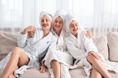 Happy friends in bathrobes with towels on couch indoors. Spa party