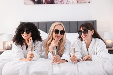 Happy friends with sunglasses and glasses of sparkling wine on bed. Spa party