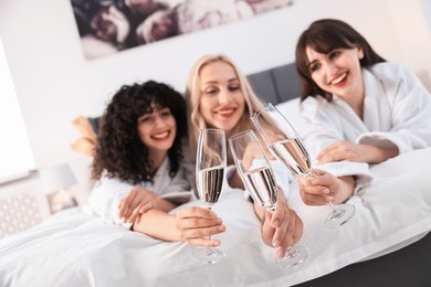 Happy friends clinking glasses of sparkling wine on bed, selective focus. Spa party