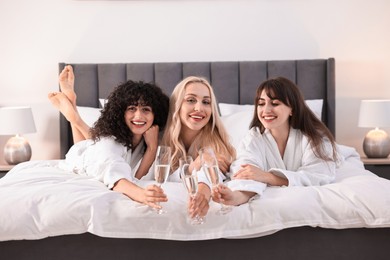 Photo of Happy friends with glasses of sparkling wine on bed. Spa party