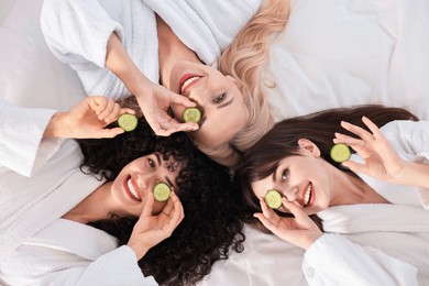 Happy friends with cucumber slices on bed, top view. Spa party