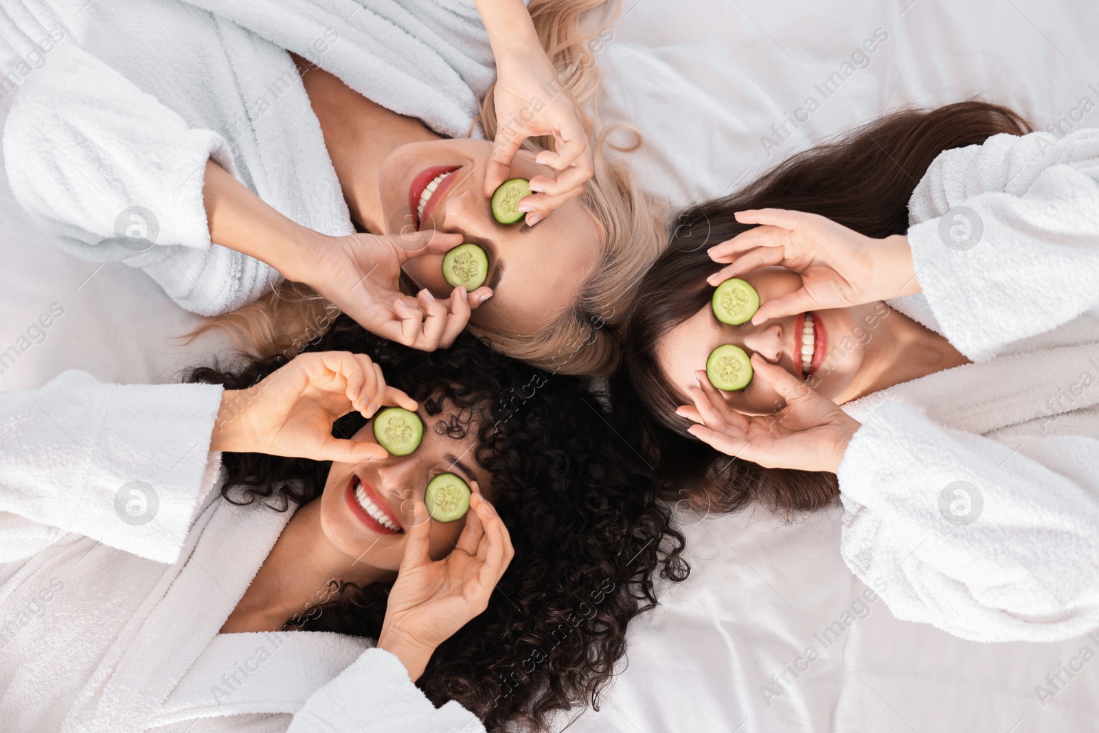 Photo of Happy friends with cucumber slices on bed, top view. Spa party