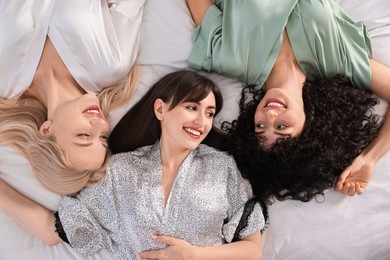Photo of Happy friends in silk bathrobes on bed, top view. Spa party