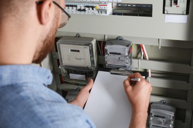 Technician worker with clipboard inspecting electricity meter, closeup