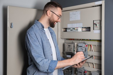 Photo of Technician worker with clipboard inspecting electricity meter indoors