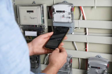 Technician worker with smartphone inspecting electricity meter, closeup