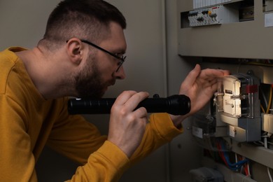 Man with flashlight checking electricity meter indoors