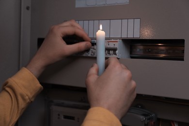 Photo of Man with candle checking electrical fuse board indoors, closeup