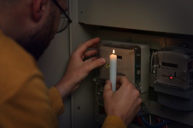 Photo of Man with candle checking electricity meter indoors, closeup