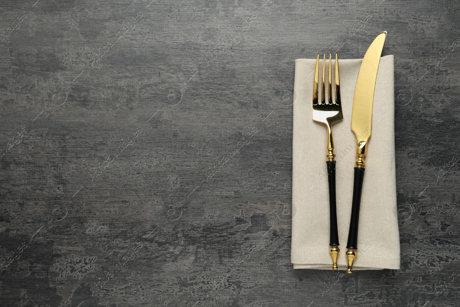 Photo of Elegant golden cutlery and napkin on grey table, top view. Space for text