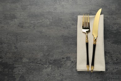 Photo of Elegant golden cutlery and napkin on grey table, top view. Space for text