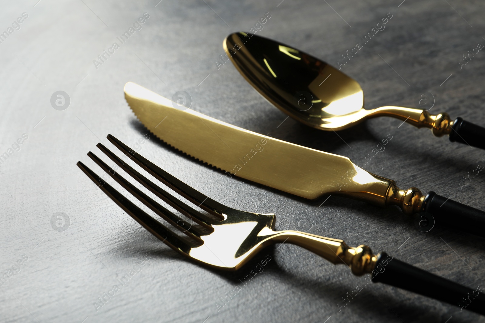 Photo of Elegant golden cutlery set on dark grey table, closeup